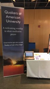a vertical banner says "Quakers at American University; A welcoming worship in silent meditative prayer; Come find the Light within yourself; Tuesdays at 8pm in Kay Chapel" next to a table with a white tablecloth